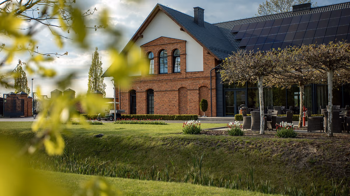 Ceglany budynek Ostoi Chobienice w wieczornym świetle, z tarasem restauracji